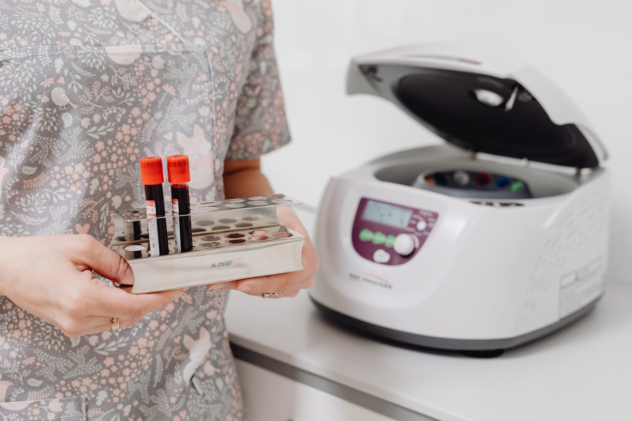 about-us Healthcare professional holding blood vials next to a laboratory centrifuge, indoors.